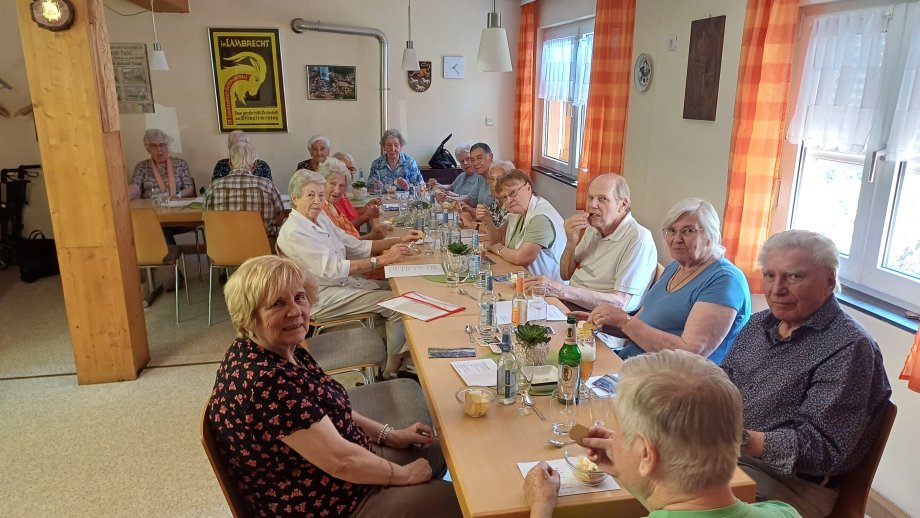 Ältere Menschen sitzen am Tisch und essen, ein paar schauen in die Kamera und lächeln.