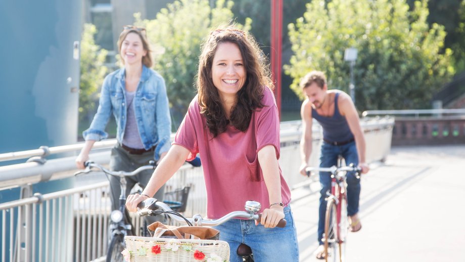 Drei Menschen fahren Fahrrad, die Radfahrerin in der Mitte lächelt in die Kamera.