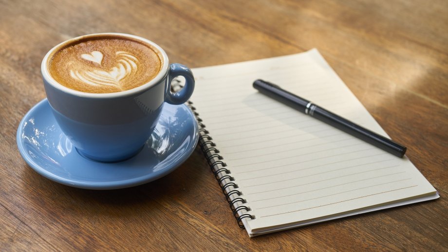 Eine Tasse mit Kaffee neben einem Notizblock mit einem Stift.