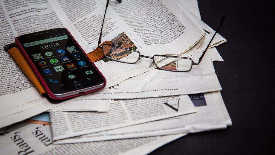 Brille und Smartphone liegen auf Zeitungen