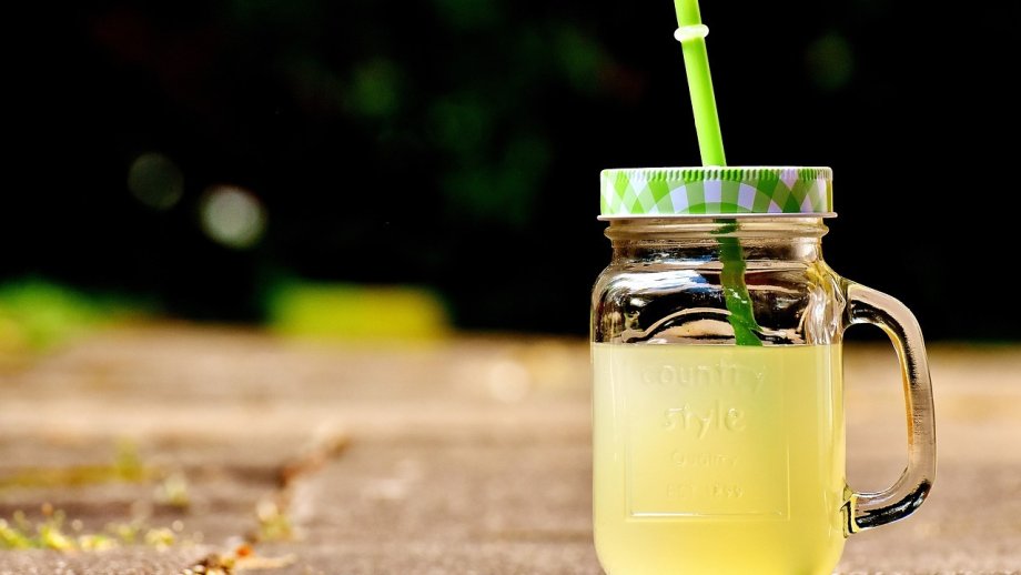 Ein Glas gelbe Limonade, das mit einem Deckel verschlossen ist, aus dem ein Strohhalm ragt. 